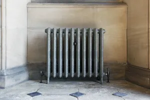 Ornate Rococo II cast iron radiator in a grey metallic finish on feet, with black angled valves, in a stone alcove with a flagstone floor.