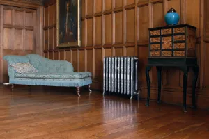 Ornate Rococo II cast iron radiator in Full Polish on feet, set against oak panelling between a blue chaise longue and a lacquered cabinet.