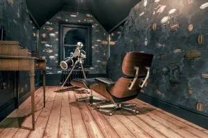 Low dark ornate cast iron radiator beneath an arched window in an attic study with balloon wallpaper, telescope, lounge chair and pine floor.