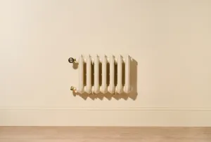 Ornate seven-column Rococo III 470mm radiator in Farrow & Ball Matchstick, wall-hung above a skirting board with Natural Brass valves.