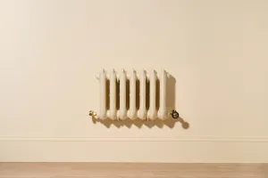 Ornate seven-column Rococo III cast iron radiator in Farrow & Ball Matchstick, wall-hung above a skirting board with Natural Brass valves.