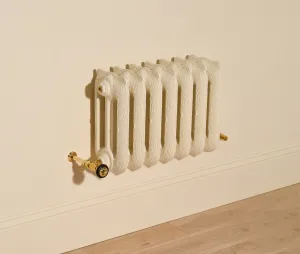 Ornate wall-hung Rococo III cast iron radiator in Farrow & Ball Matchstick with Natural Brass valves, above a skirting board and oak floor.