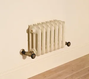 Ornate Rococo III cast iron radiator in Farrow & Ball Matchstick No. 2013, wall-hung above a skirting board with Natural Brass valves.