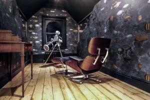 A low Rococo III 470mm cast iron radiator beneath an arched attic window, with airship wallpaper, a telescope, a lounge chair and pine floorboards.