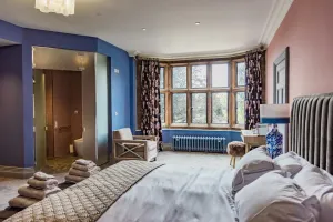 Low Rococo III cast iron radiator in blue on feet beneath a mullioned bay window in a bedroom with blue walls and floral curtains.