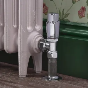 Chrome Niva angled thermostatic valve on the foot of a pale pink cast iron radiator, against a green skirting and floral wallpaper.