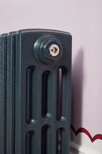 Close-up of a Castrads bleed valve on the end section of a plain Grace 4 Column cast iron radiator in Anthracite against a lilac wall.