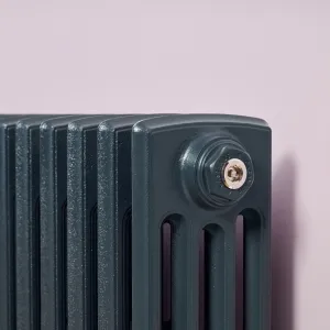 Close-up of a plain four-column cast iron radiator in Anthracite with a chrome bleed valve in a Castrads end plug, against a lilac wall.