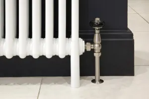 Close-up of a white Florence 3 column steel radiator leg beside a brushed nickel angled valve with black head, against a dark navy wall.