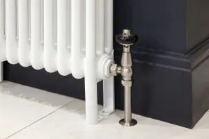 Close-up of a white Florence steel column radiator with a satin nickel valve and black wheel head, against a dark navy wall and skirting on a pale tiled floor.