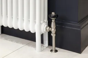 Close-up of a white Florence steel column radiator on feet with a satin nickel angled valve and black head against a dark navy skirting board.