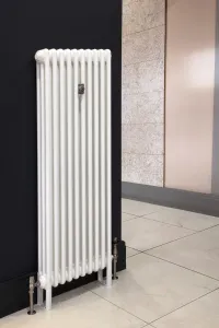 Tall white Florence 3 Column steel radiator on feet against a navy wall, with a wall stay, brushed metal valves and a pale tiled floor.