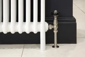 Close-up of a white Florence 3 column steel radiator on floor-standing legs, with a brushed nickel angled valve against a dark painted skirting.