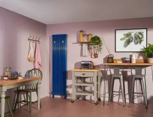 A tall blue Florence 3 column 1800mm steel radiator, wall-hung with valves, in a pink kitchen beside a butcher's trolley and breakfast bar.