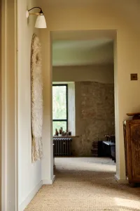 View down a sisal-carpeted landing to a Grace 4 Column radiator in Grey Bronze beneath a steel window beside a bare stone wall.