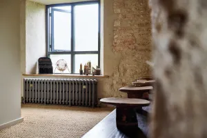 Plain Grace 4 Column 500mm cast iron radiator in Grey Bronze on feet beneath a window in a stone-walled room with sisal flooring.