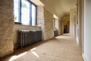Grace 4 column cast iron radiator in Grey Bronze on feet beneath a window in a stone-walled landing with sisal carpet, a second one beyond.