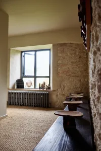 Grace 4 Column 500mm cast iron radiator in Grey Bronze under a window in a stone-walled room with sisal carpet and a wooden bench.