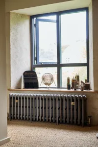 Grace 4 Column 500mm cast iron radiator in Grey Bronze on feet beneath a deep window sill, with brass valves and sisal flooring.