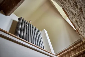 Grace 4 Column 760mm cast iron radiator in Grey Bronze on a stair landing, seen from below beside a stone wall and timber beam.