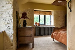 Grace 4 Column cast iron radiator in Grey Bronze beneath a window in a stone-walled bedroom with sisal carpet and a cane bed.