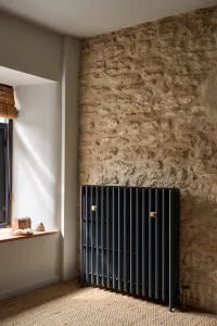 Grace 4 Column 960mm cast iron radiator in Midnight Ink on feet against an exposed stone wall, beside a window on sisal carpet.
