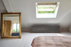 Low Grace 6 Column cast iron radiator in Grey Bronze with brass valves, under a skylight in an attic bedroom with white floorboards and a gilt mirror.