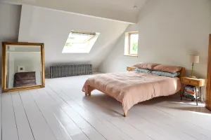 A low Grace 6 column cast iron radiator in Grey Bronze under a roof window in a loft bedroom with white painted floorboards and a linen-covered bed.