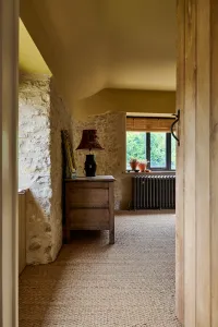 Grace 4 Column 660mm cast iron radiator in Grey Bronze on feet beneath a window, beside stone walls, an oak chest and sisal flooring.