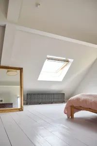 Low Grace 6 Column cast iron radiator in Grey Bronze on feet beneath a roof window in an attic bedroom with painted floorboards.