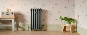 Grace 4 column cast iron radiator in Pencil with Windsor angled TRV, against seagull wallpaper and sage skirting on a wooden floor.
