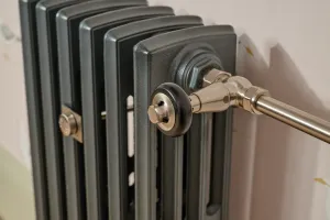 Close-up of a plain Grace four-column cast iron radiator in a dark grey finish, with a nickel Windsor angled valve and a wall stay.
