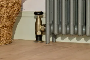 Close-up of a plain Mercury cast iron radiator foot in Quartz Grey with a brass Windsor angled valve, beside a woven basket on an oak floor.