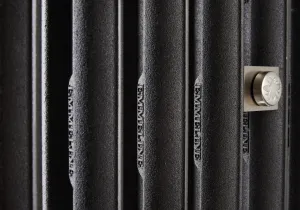 Close-up of Emmeline cast iron radiator columns in a dark textured finish, with the Emmeline name cast in and a brushed nickel square fitting.
