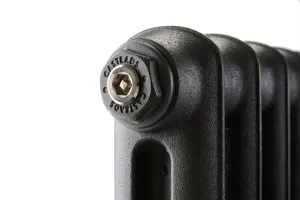 Close-up of the top corner of an Emmeline cast iron radiator in a black finish, showing a Castrads-embossed end plug with a hex bleed valve.