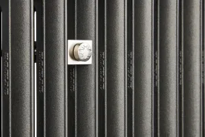 Close-up of Emmeline II cast iron radiator columns in a textured Black Iron finish, with a square nickel fitting embossed with a bee.