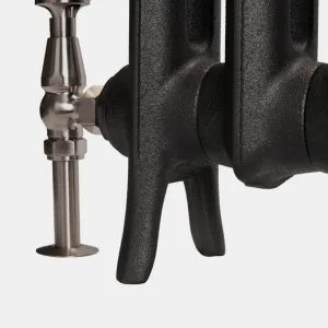 Close-up of the feet of an Emmeline cast iron radiator in textured Matt Black, with a satin nickel angled valve and floor pipe shroud.