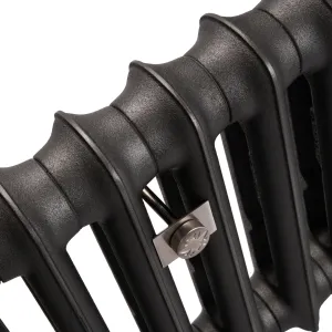 Close-up of an Emmeline I cast iron radiator in Matt Black, showing its textured columns and a brushed metal wall stay between sections.