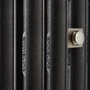 Close-up of Emmeline cast iron radiator columns in a textured black finish with cast lettering and a satin nickel bee-motif fitting.