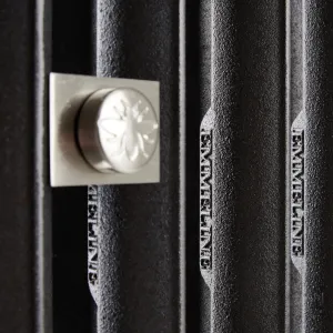 Close-up of black Emmeline cast iron radiator columns with raised EMMELINE lettering and a satin nickel square fitting embossed with a bee.