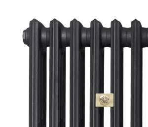 Close-up of the top of a Grace 4 Column cast iron radiator in a dark charcoal finish with a brass bee emblem plate, on white.