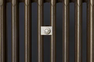 Close-up of plain columns on a Mercury cast iron radiator in Beaten Brass, with a pale metal plaque bearing an embossed bee emblem.