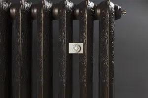 Close-up of an ornate Rococo II cast iron radiator in a dark bronze finish, with a square floral wall stay and a brass bleed valve, on a dark grey background.