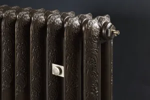 Close-up of an ornate Rococo II cast iron radiator in a dark bronze finish, with a brass bleed valve and a round wall stay plate.