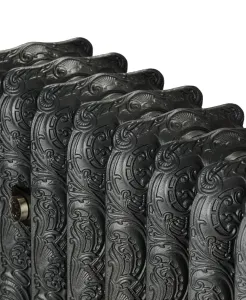 Close-up of ornate Rococo III cast iron radiator sections with scrolled shell relief in a dark metallic iron finish, a nickel fitting at the side.