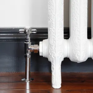 Chrome Crosshead angled manual valve on a floor pipe, connected to an ornate white cast iron radiator on feet, dark skirting and wooden floor.