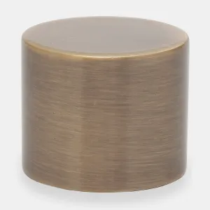 Plain cylindrical Niva lockshield cap in a brushed Antique Brass finish with a slightly bevelled top, shown against a pale grey background.