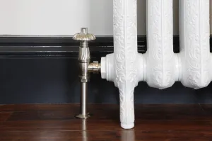 Chatsworth angled TRV in Satin Nickel on an ornate white cast iron radiator on feet, beside a dark skirting board and wooden floor.