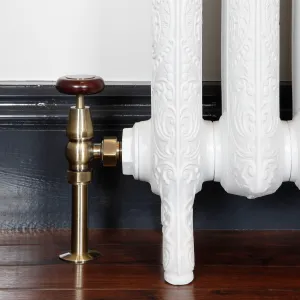 Windsor angled manual valve in Antique Brass with a wooden head, fitted to the foot of an ornate white cast iron radiator on a dark wood floor.