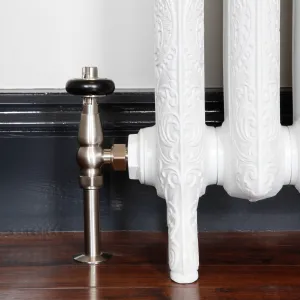 Windsor angled thermostatic valve in Satin Nickel with black head on an ornate white cast iron radiator foot, by a dark skirting and wooden floor.
